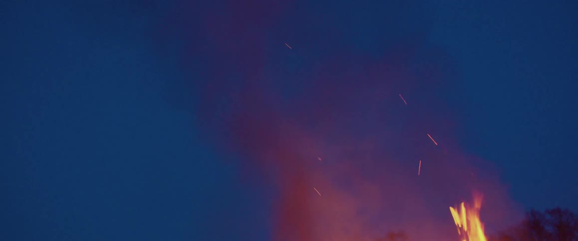 Bonfire smoke and sparks floating up the dark blue evening sky