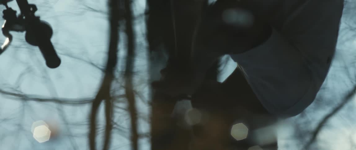 A puddle of water shows the reflection of a man smoking a cigarette near trees