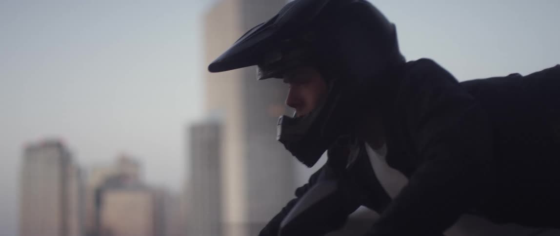 Man rides motorcycle over bridge as a view of the city is seen through the structure