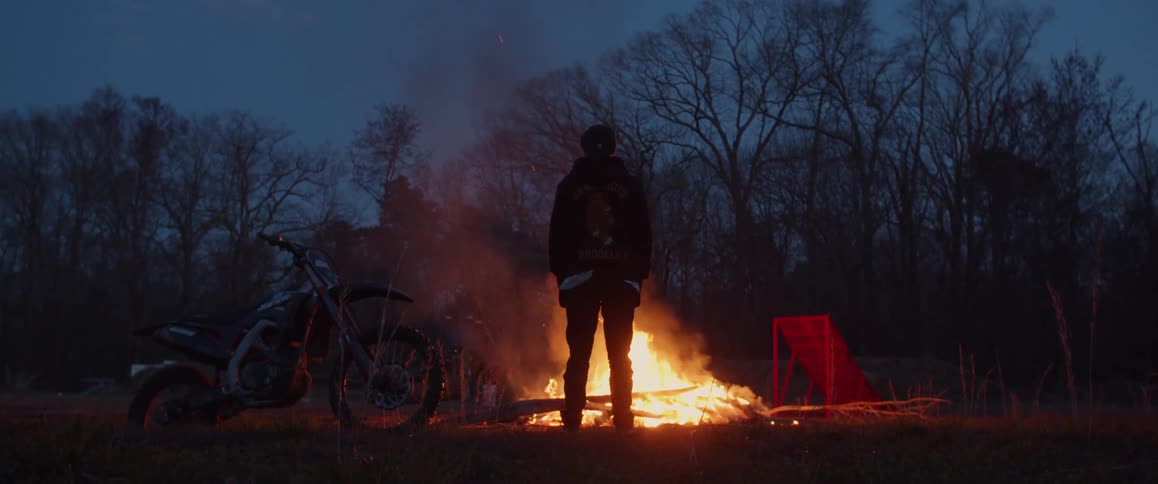 A man stands next to his bicycle and watches a fire burn in the forest