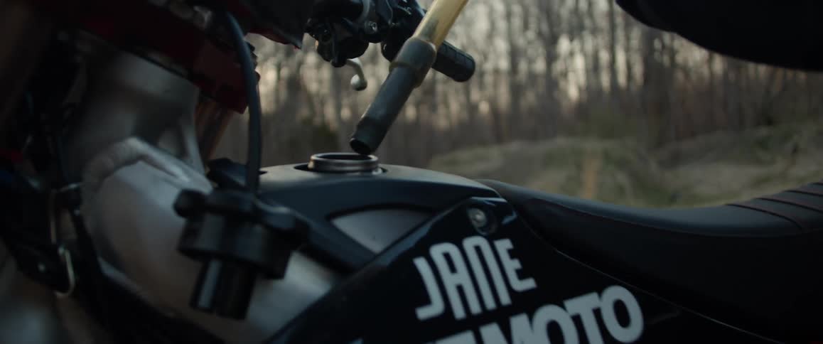 A man lifts up a jug and puts gas in to his motorcycle