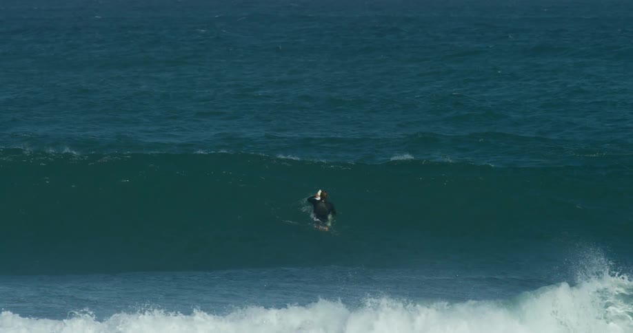 Male surfer wearing wet suit paddles over waves while lying on surfboard