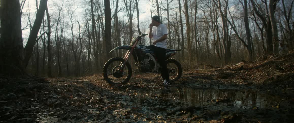 A man sits on a motorcycle in the woods