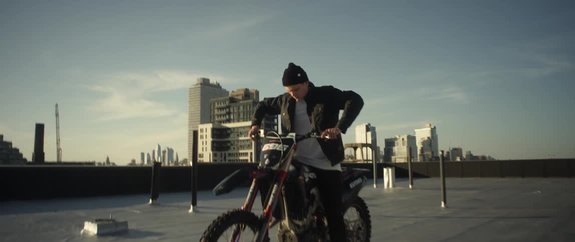 A man on a rooftop sits on a motorcycle and pushes on the handles