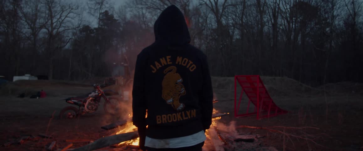 A man is standing in the dark looking at a bonfire