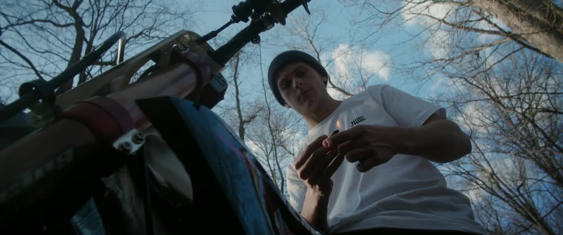 A teenager sitting on a motorcycle holds a small flame above his hand