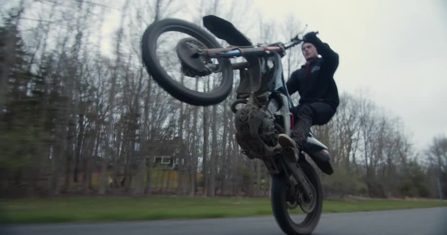 A man drives his motorcycle down a neighborhood street and then does a wheelie