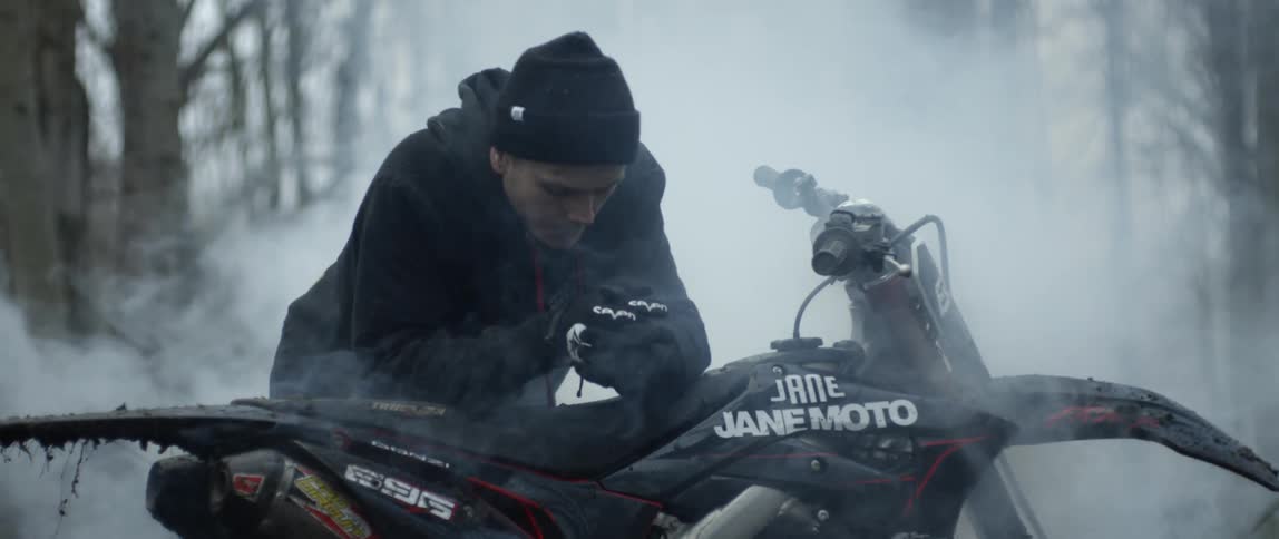 A man is leaning on his dirt bike surrounded by smoke