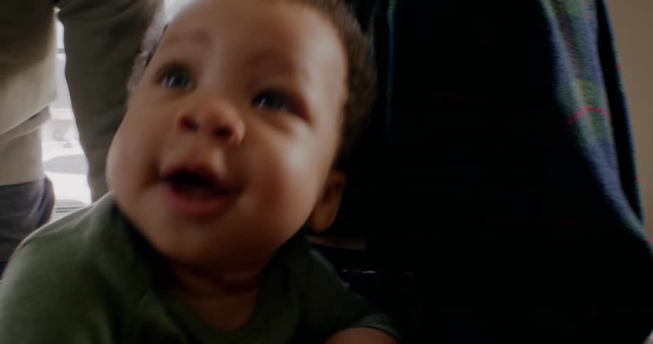 One adult stands while another holds baby on their lap