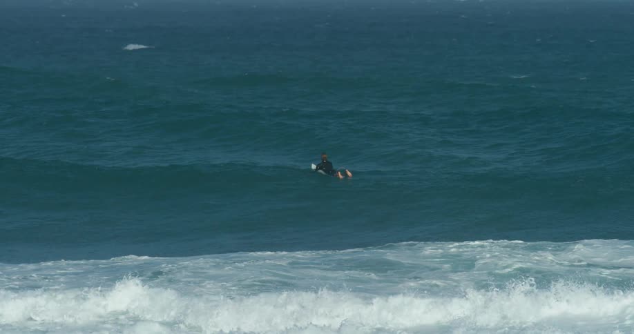 Surfer wearing black wet suit floatin on a surfboard over the ocean waves