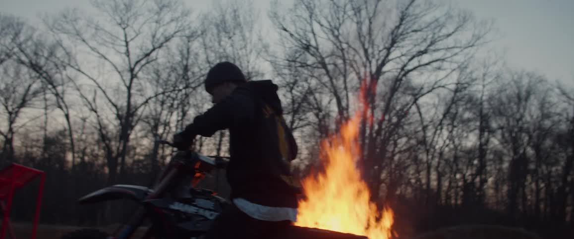 A man parks his motorcycle near a bonfire and walks away