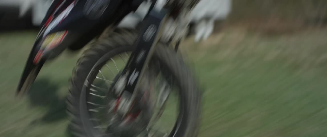 A man does a wheelie on an off road motorcycle in a field during the day