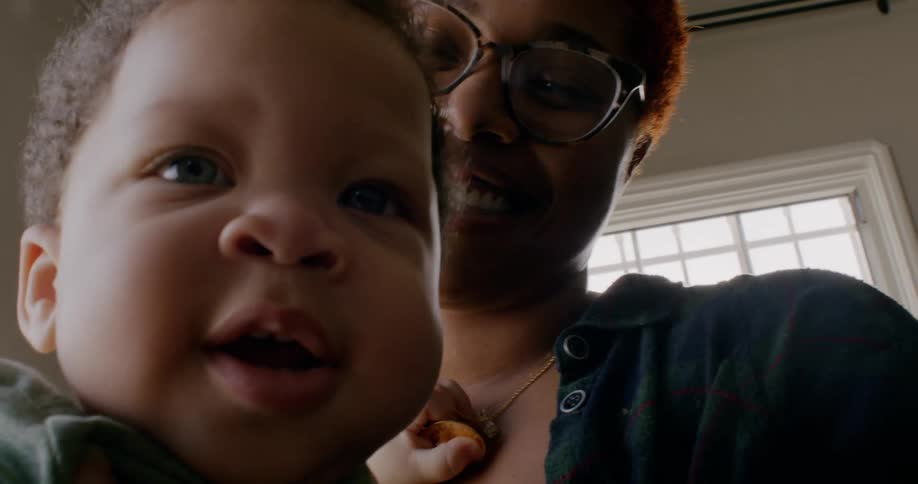 Mother holds child smiling as he hides his face against her