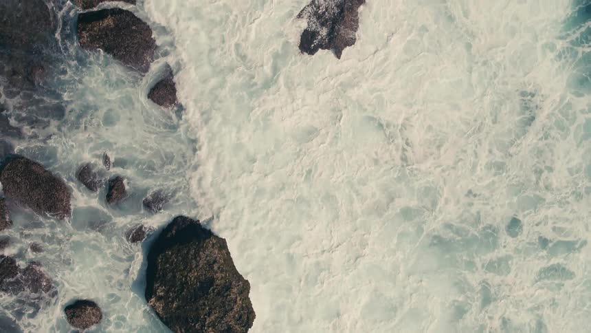 Areial view of waves crashing into rocks as they roll into shore