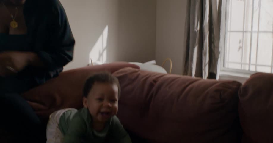 A woman puts her baby on a couch and watches as he laughs and tries to crawl forwards