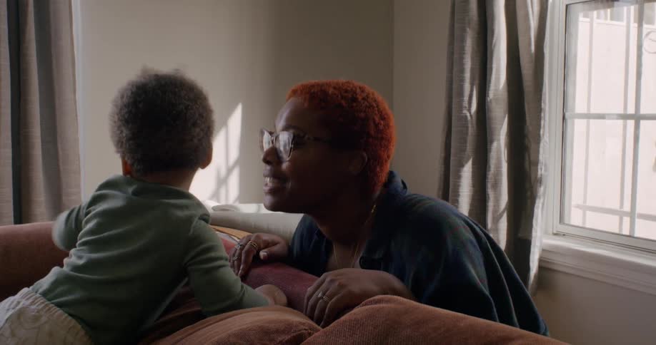 Mother crouches down to play with child on couch
