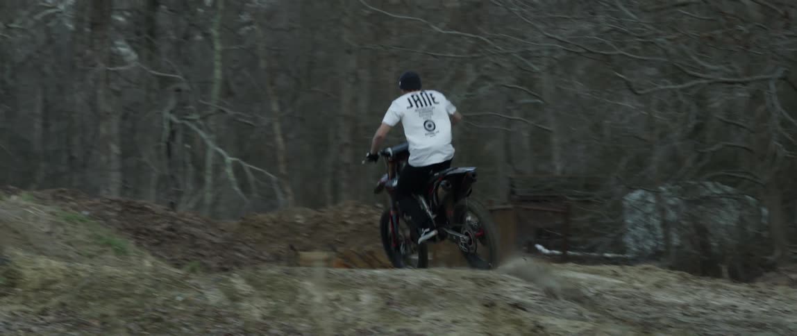 A man rides a motorized bicycle up and down hills near a forest