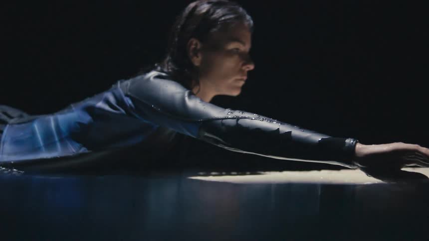 A woman is surfing on the water at night