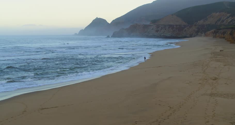 Waves roll over the sand as someone runs along the beach