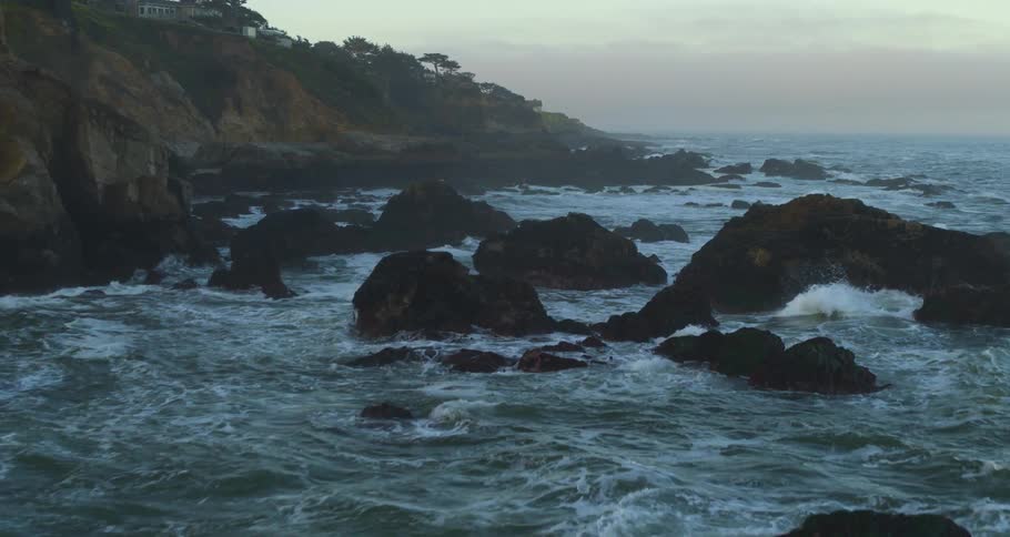 Ocean waves are flowing up onto a rocky beach near coastal cliffs