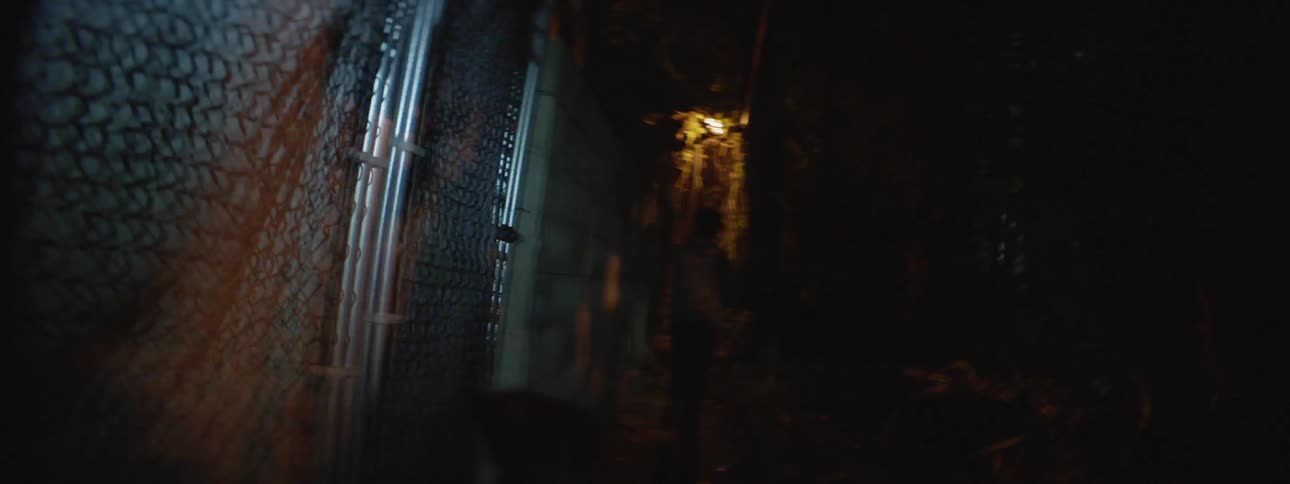 First person view running through a dark alleyway surrounded by a chain link fence