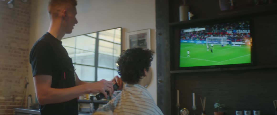 Barber and boy in barber chair watch soccer game