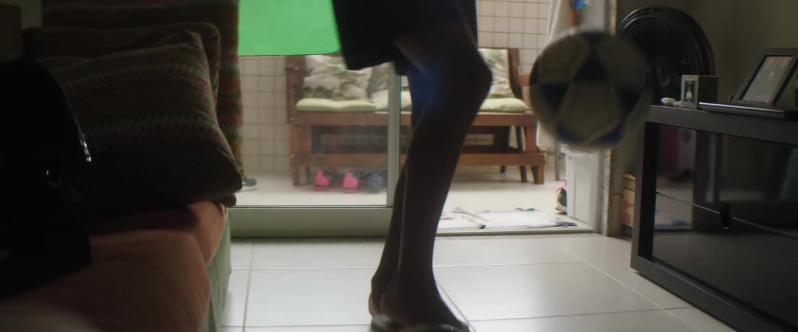 Teen boy with shorts and flip flop juggles ball in living room at home