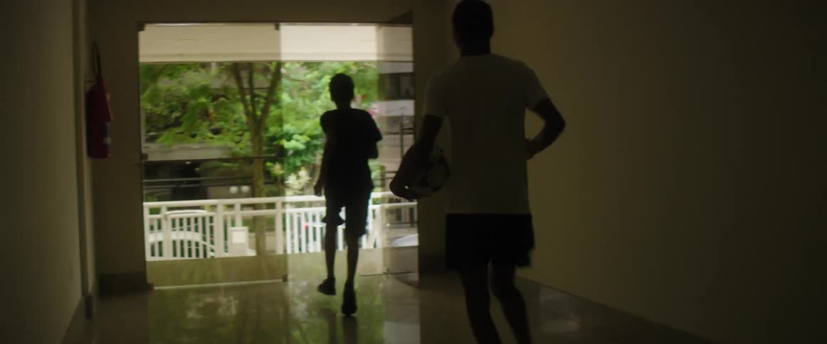 A man and child run out of a building with a soccer ball