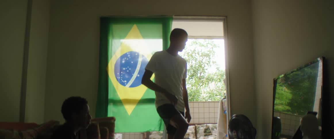 Boy sitting on couch and teen boy putting foot on ball watch football television in living room at home