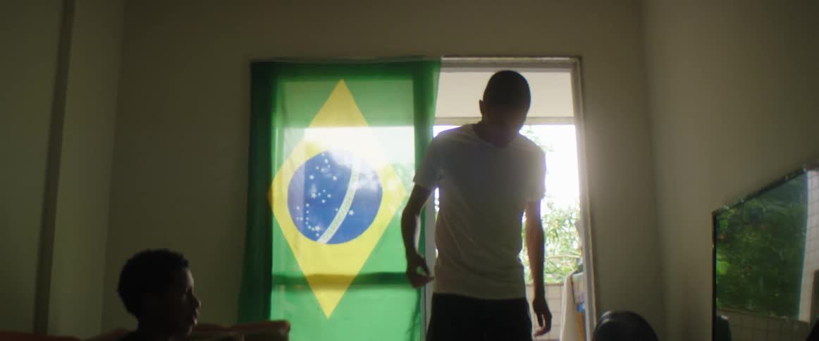 Silhouette of a young man playing with a soccer ball inside an apartment near a brazil flag