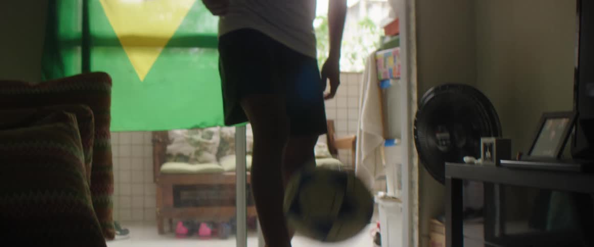Silhouette of a young man playing with a soccer ball in front of a brazil flag inside an apartment