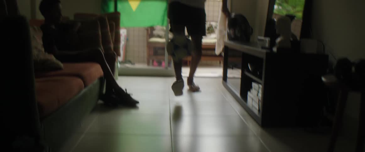 A boy kicks a soccer ball in the living room as another watches television