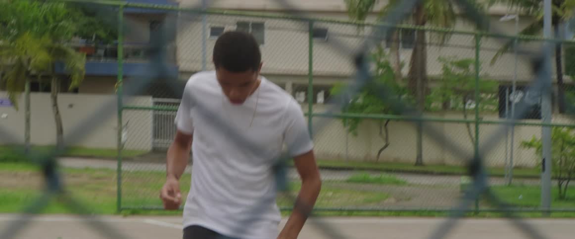 A young man juggles a soccer ball with his feet on an outdoor basketball court during the day