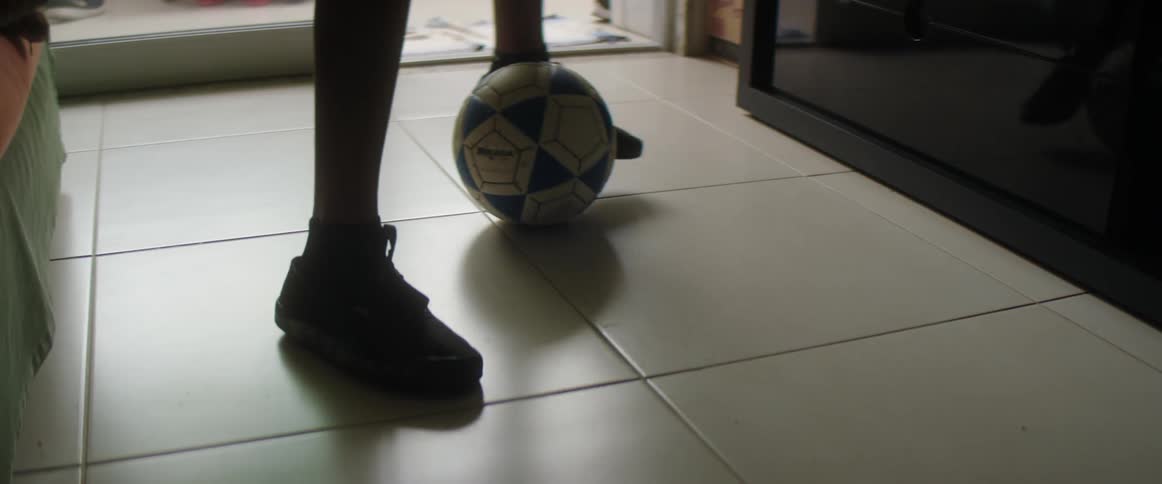 A boy is dribbling a soccer ball indoors