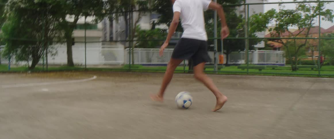 A teenager runs barefoot as he kicks a soccer ball into the goal