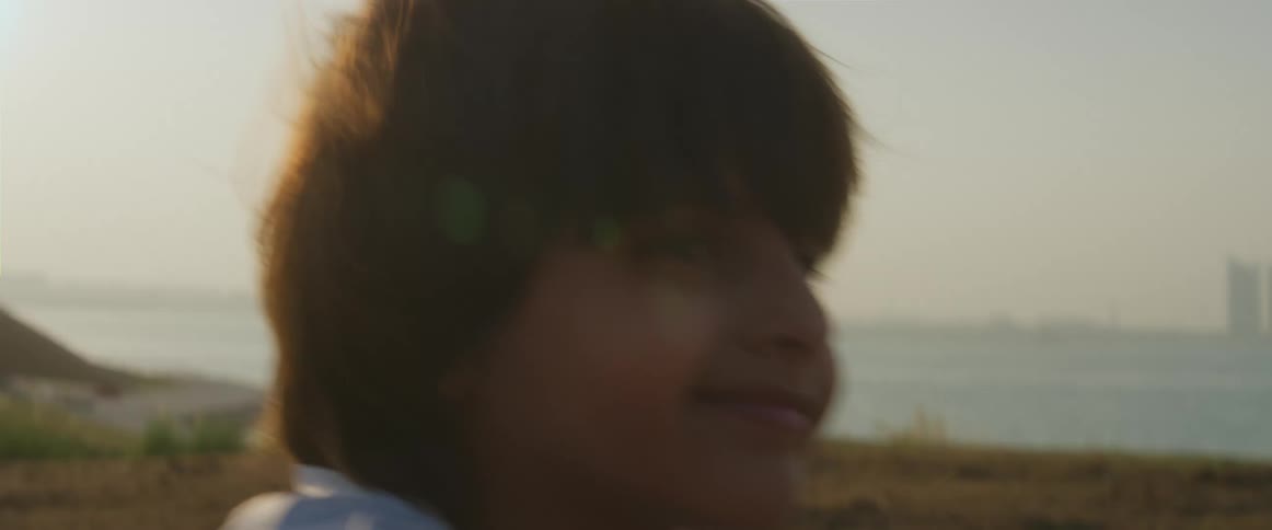 A boy smiles as he sits in a field near the sea