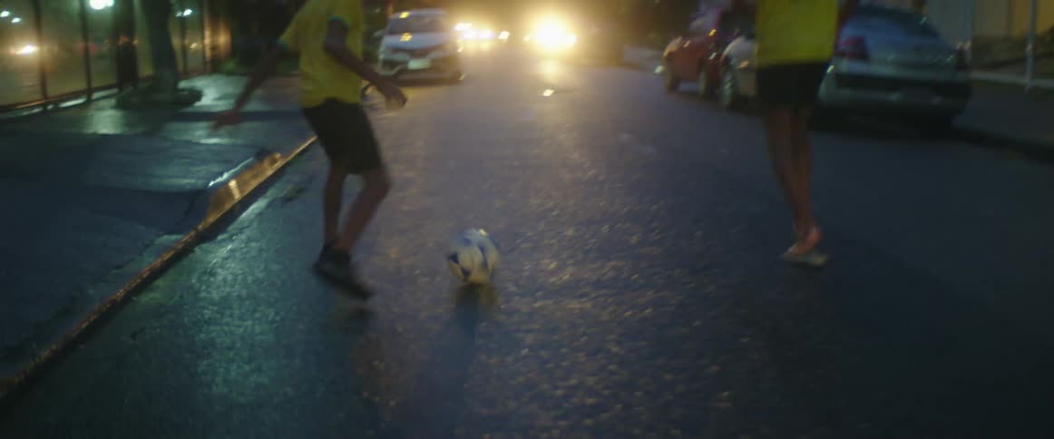Three teenage boys run down a neighborhood street kicking a ball back and forth