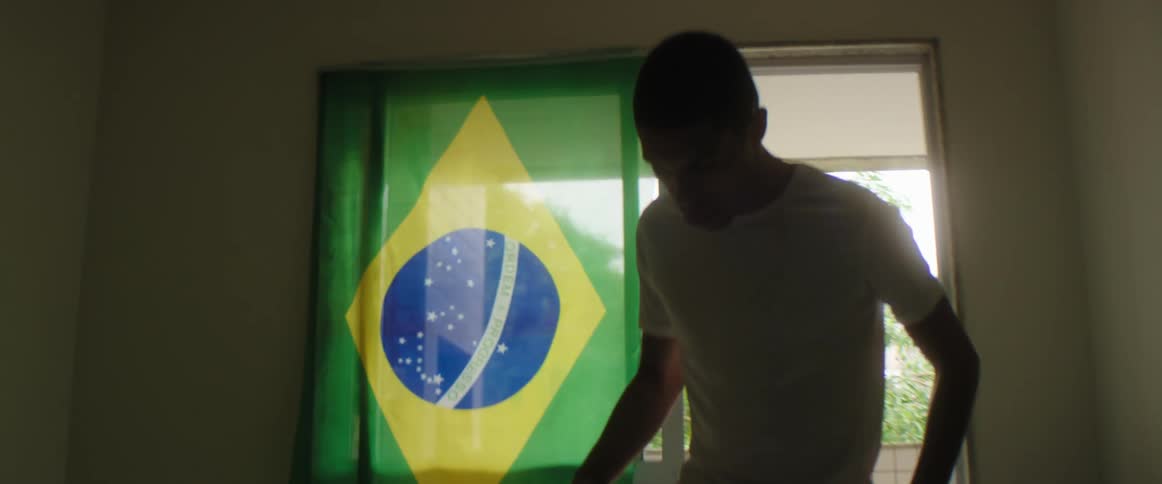 Teen boy wit white t shirt and black pants juggling soccer ball is silhouetted in living room at home