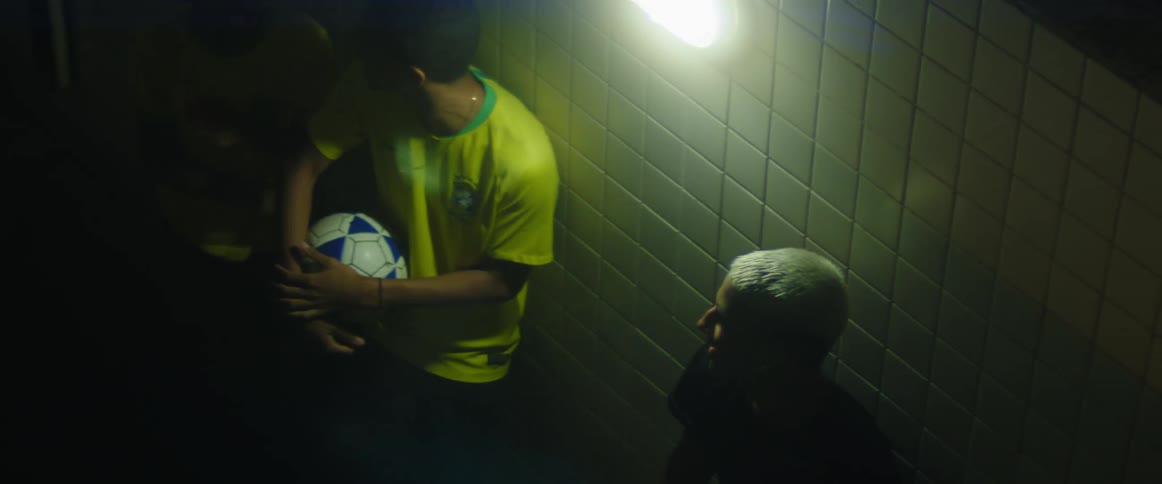 Friends one holding a soccer ball joke around near tiled wall lit by light at night