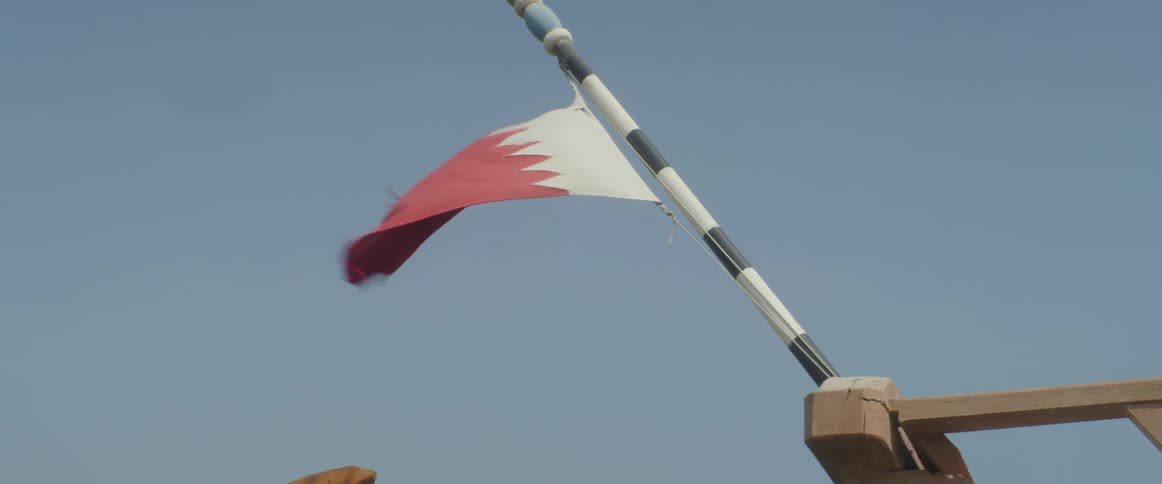 National flag of qatar waving in the wind on a flagpole under the blue sky