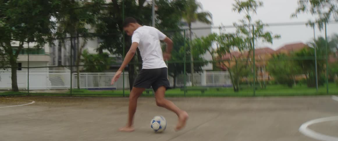 A teenager runs barefoot as he kicks a soccer ball into a goal