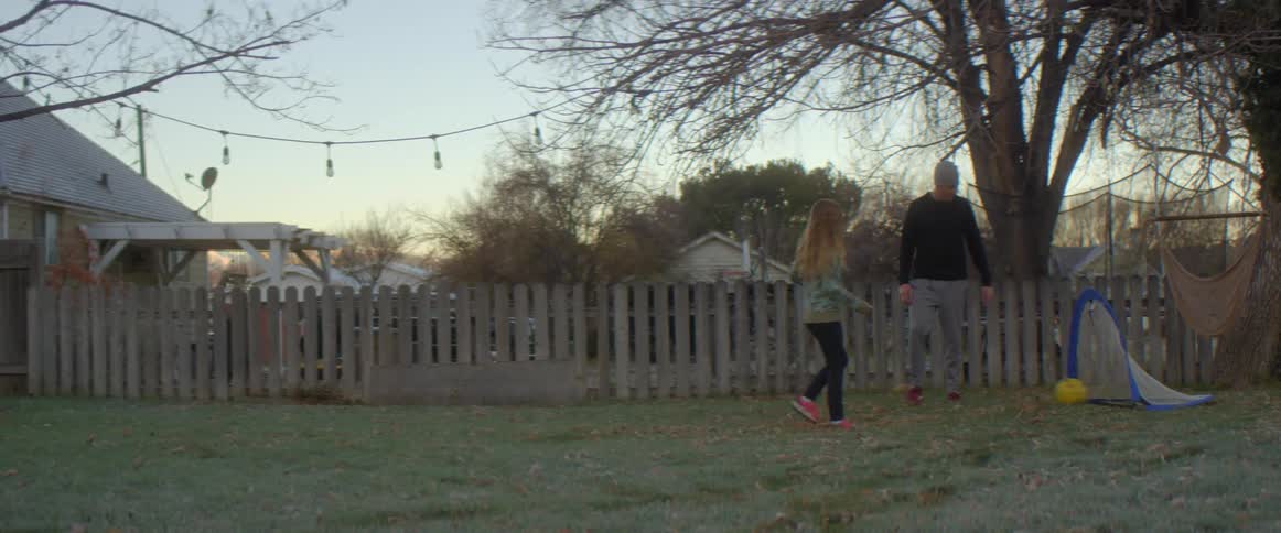 A young girl kicks a soccer ball into the net as her father watches