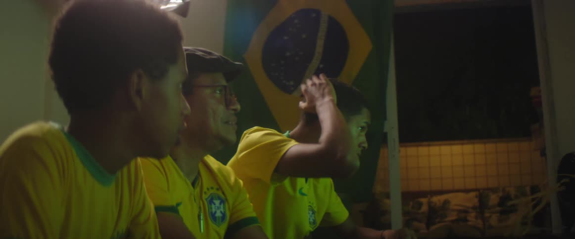 Father and sons wearing brazilian football uniform watch football match on television in living room at home