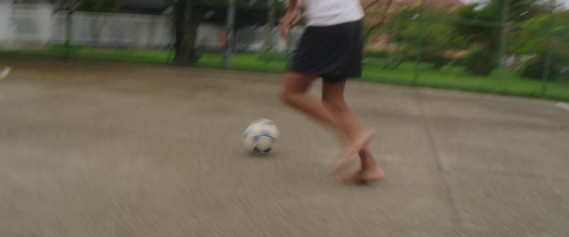 A teenager is doing feet tricks with a soccer ball as he approaches a goal then kicks the ball in