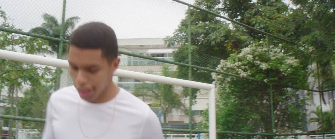 A barefoot young man juggles a soccer ball with his feet on a cement soccer field on a cloudy day