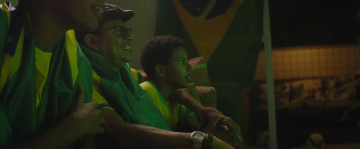 A group of people sitting on couch wearing brazil football uniform watches football on television