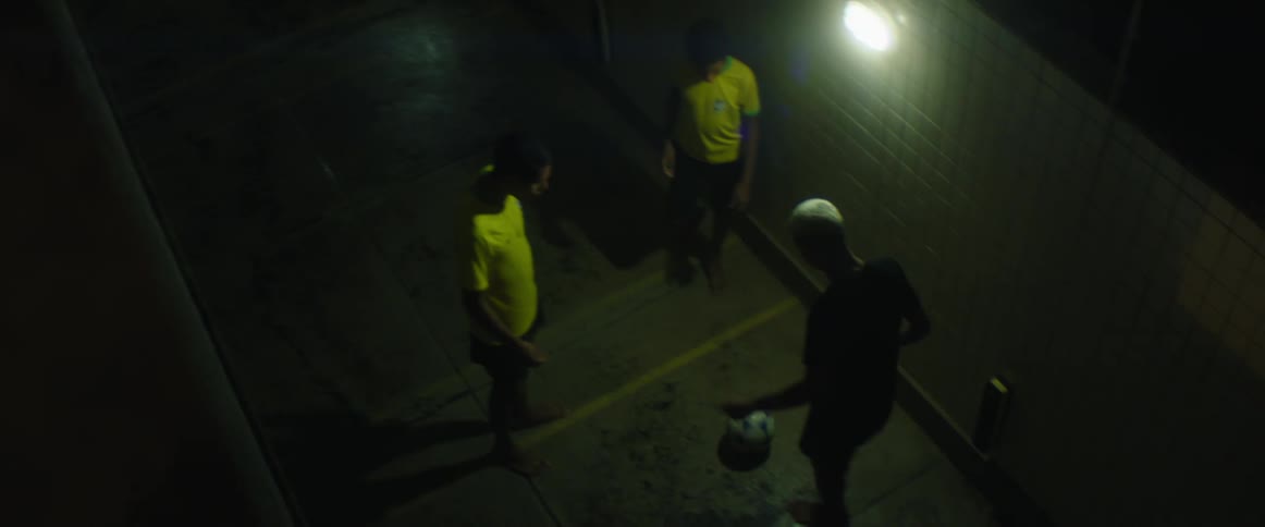 Three men play with soccer ball standing in alley near light