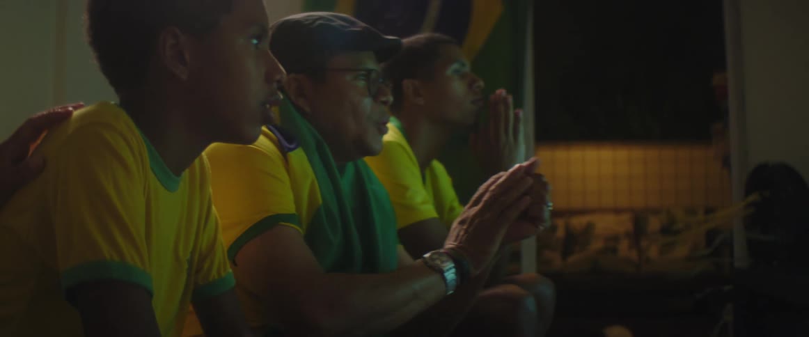 A pair of men and a boy watch sports together while sitting in a dark room