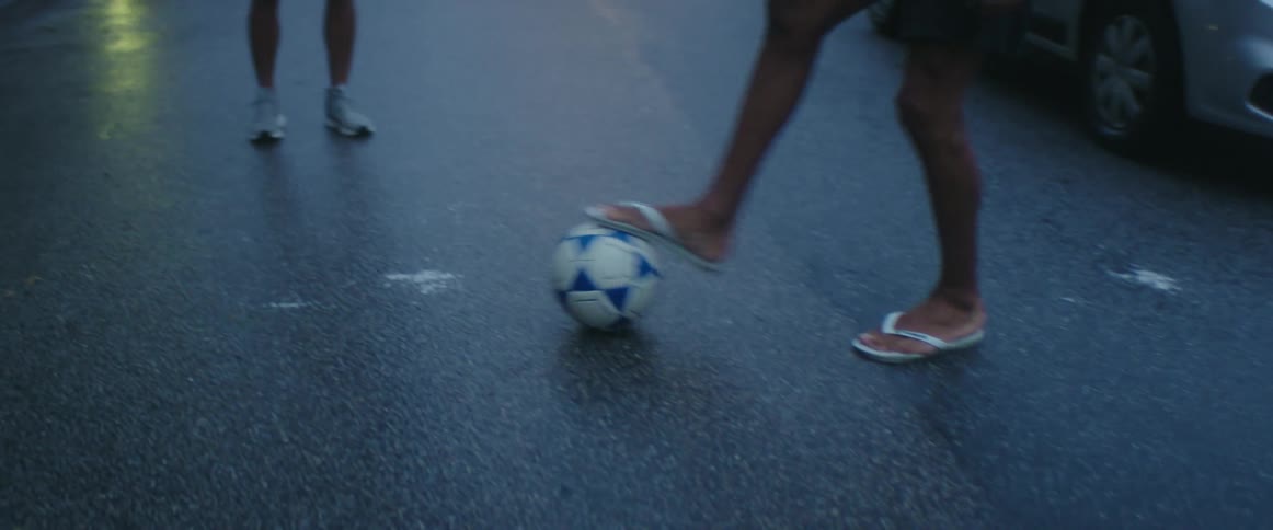 A group of young males kick a soccer ball to each other standing in the street