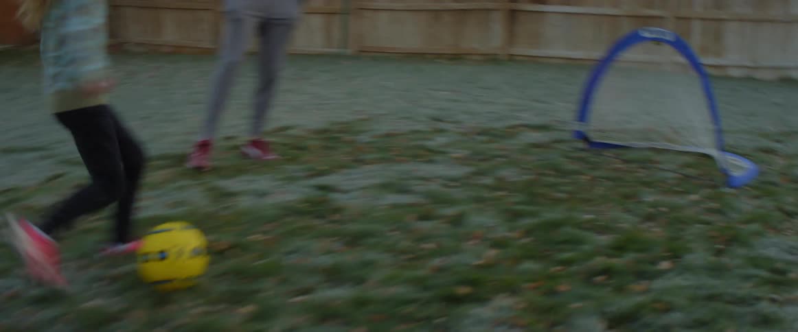 Fair haired girl dribbles soccer goal to small goal in yard as father watches